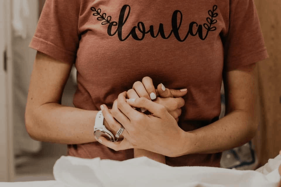 Women in doula shirt holding the hand of a woman in labor at Bliss Birth and Fertility Center in West Palm Beach