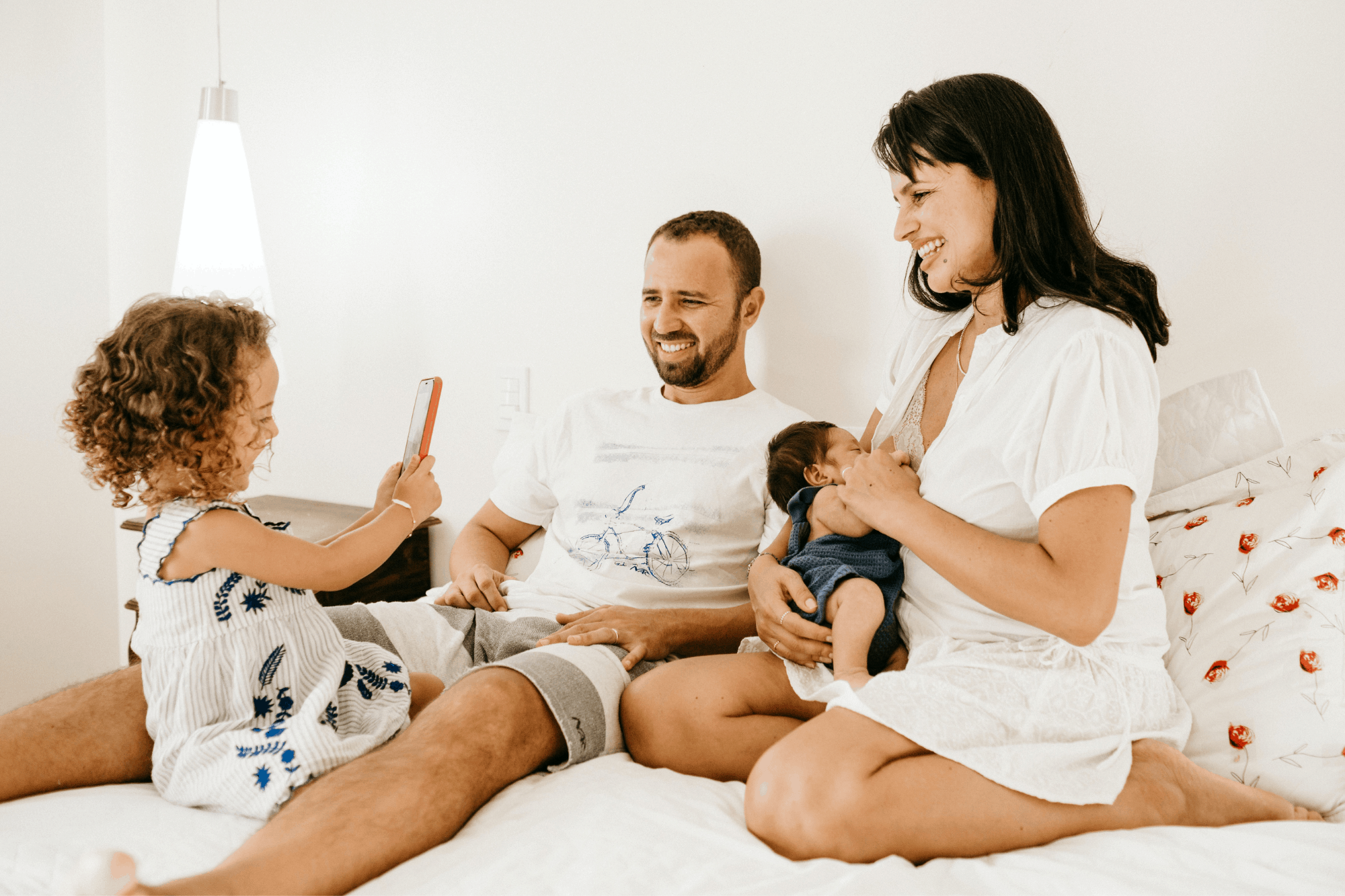 Family with newborn on a bed smiling after parenting classes at Bliss Birth and Fertility Center in West Palm Beach
